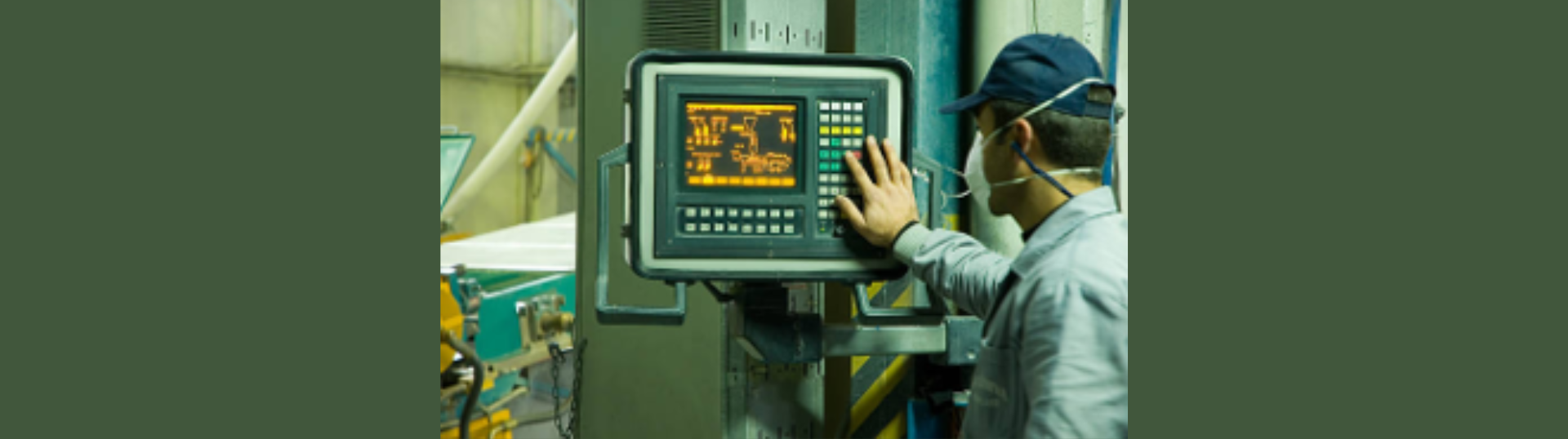 A row of large green industrial machines sits inside a manufacturing facility, surrounded by wooden crates and metal bins. Yellow floor markings outline walkways, and hydraulic hoses and control panels are visible on the equipment.
